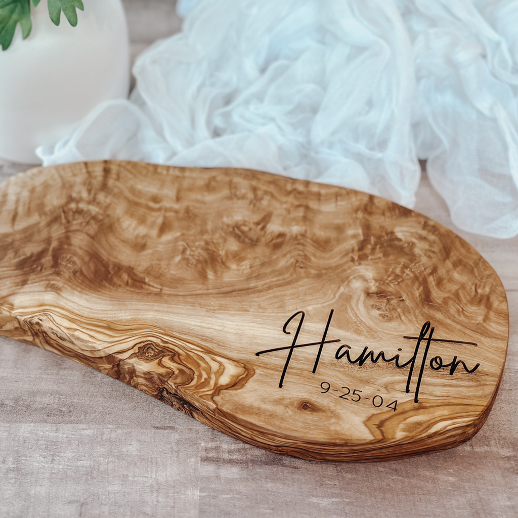 Personalized live-edge olivewood cutting board engraved with a custom name and date, styled for a wedding